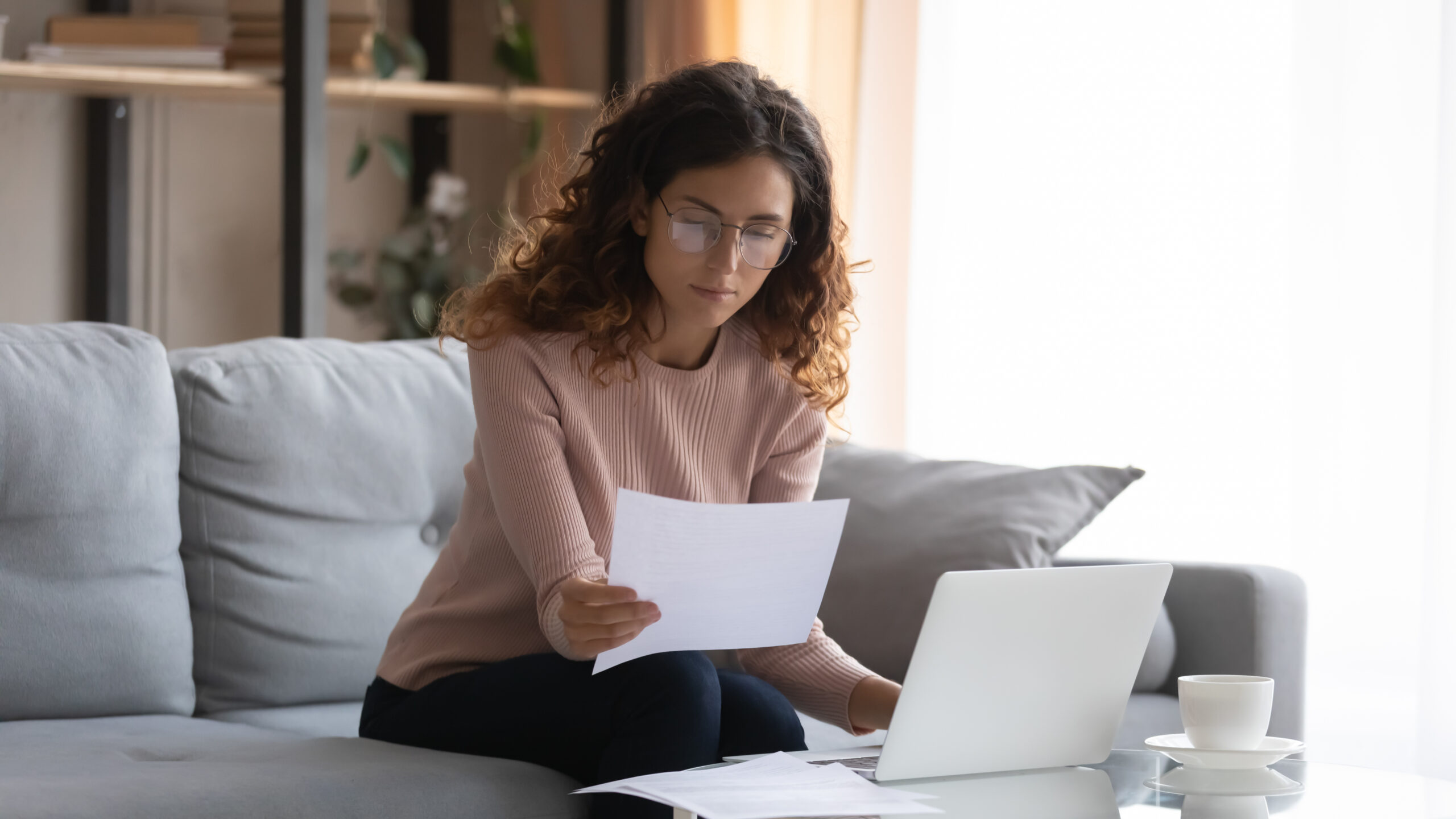 Young Caucasian woman work on laptop considering paperwork